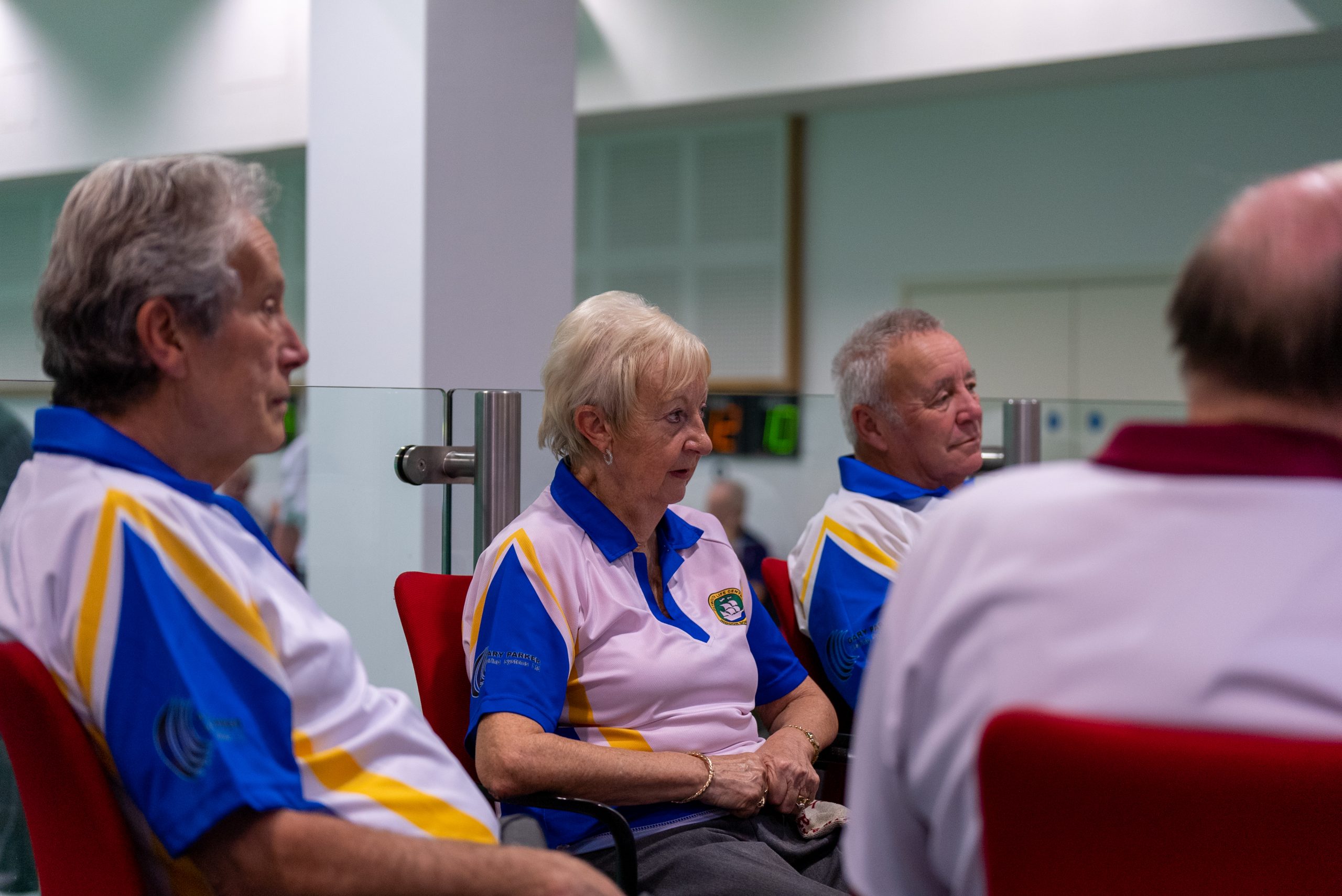 Three elderly people wearing a bowls club uniform looking right.